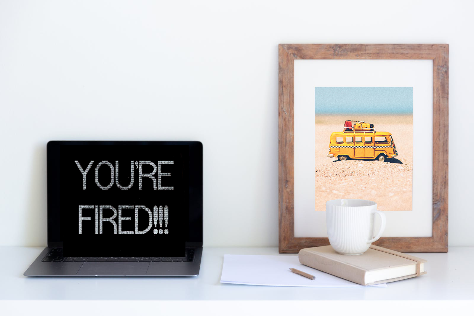 Laptop mit Text 'You're Fired' und Bilderrahmen mit Urlaubsmotiv