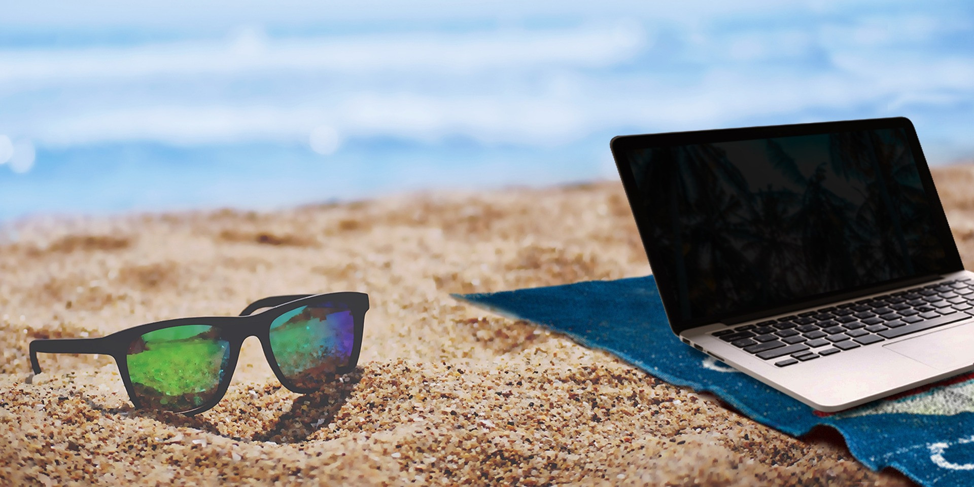 Sonnenbrille und Laptop am Strand